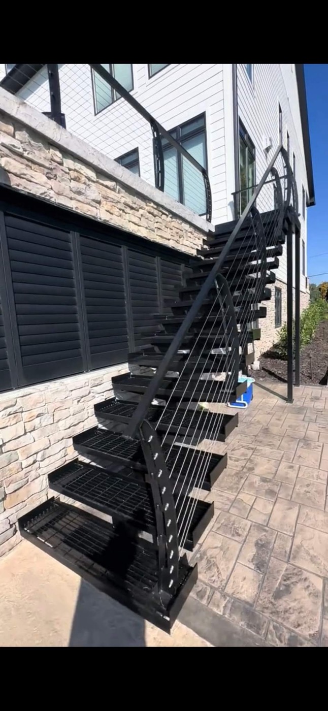 Exterior black metal staircase with cable rail over pavers
