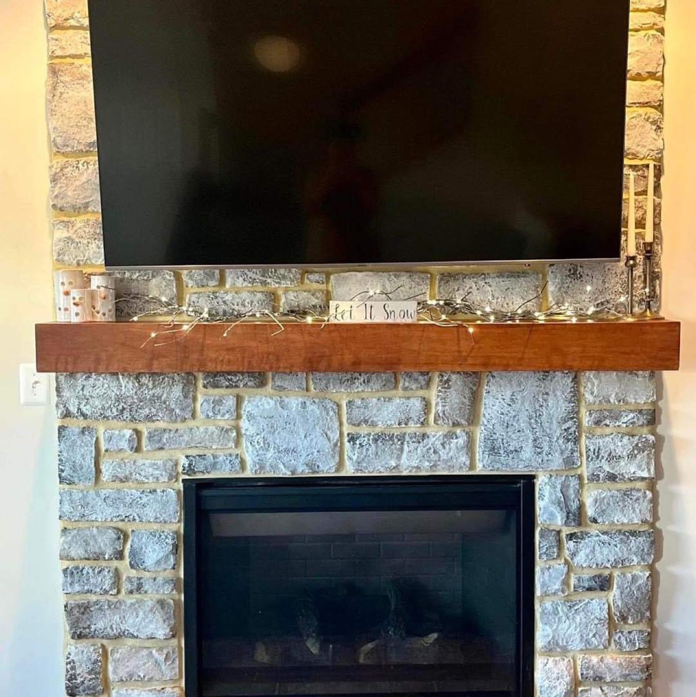Stone fireplace wall with TV and wood mantel