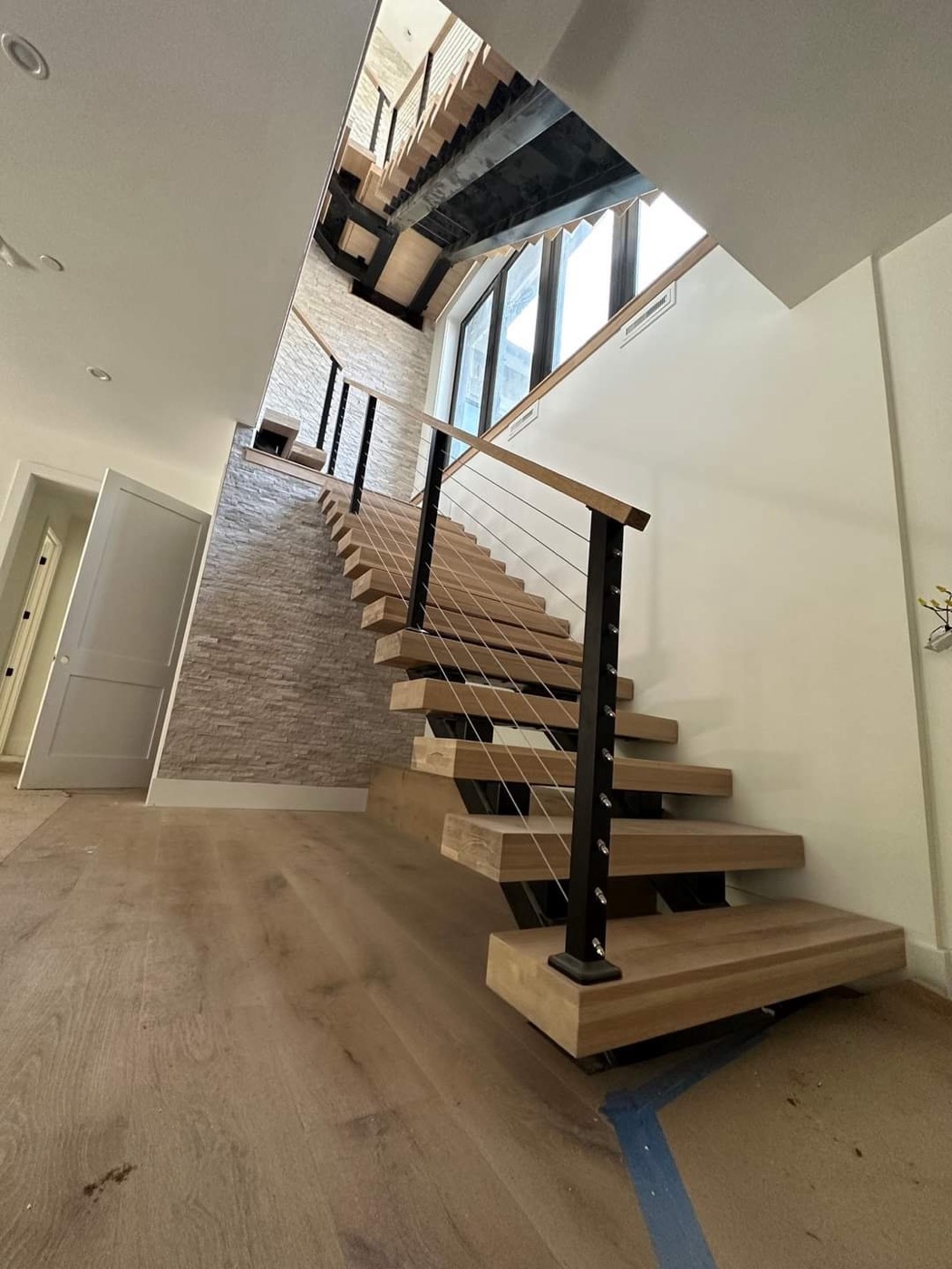 Light wood floating staircase with black stringers and cable rail
